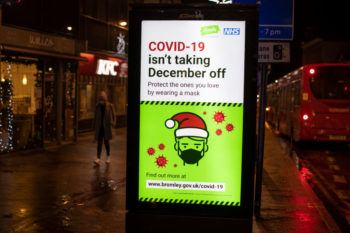 a sign reading "covid-19 isn't taking december off" displayed outside along a row of shops in england