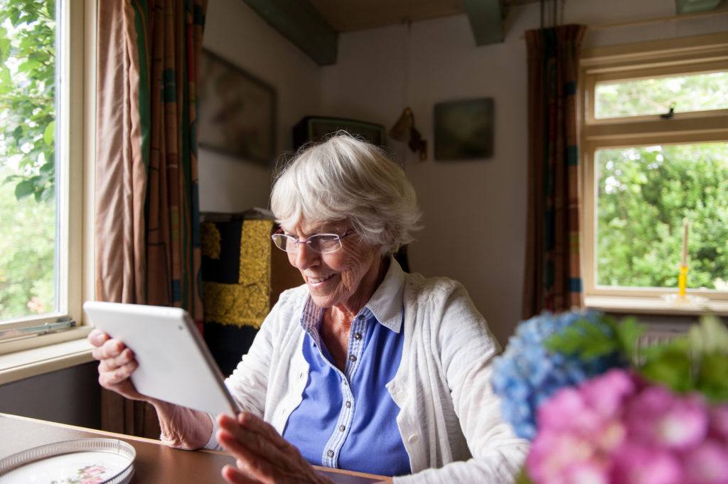 an elderly woman uses a tablet in her kitchen