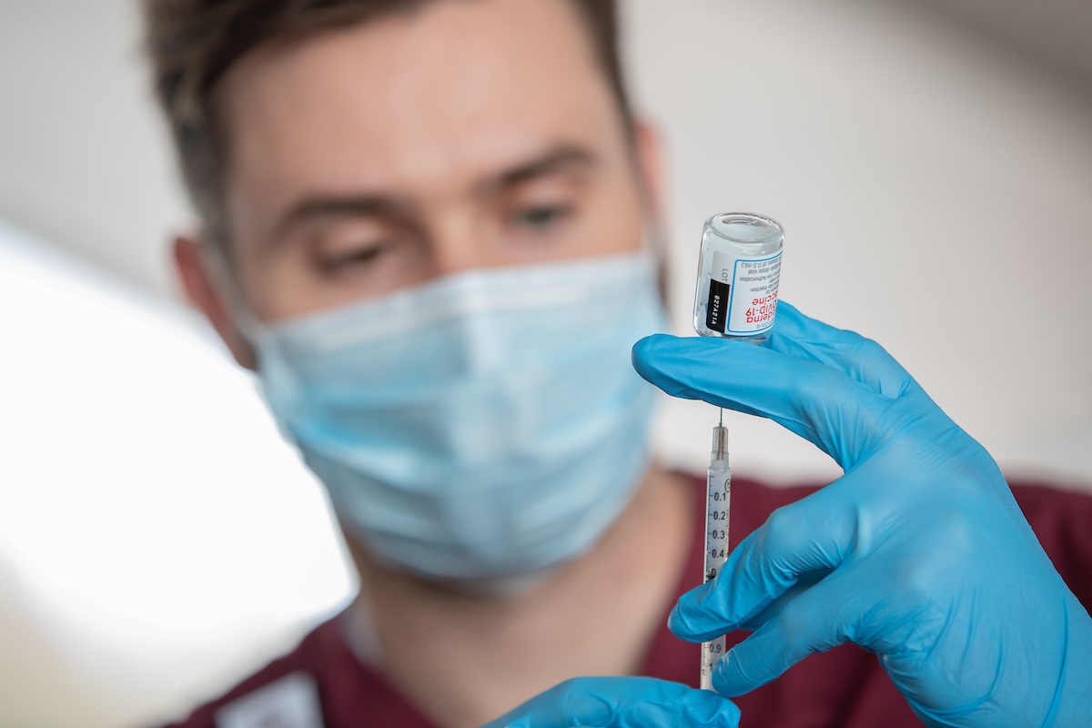nursing student putting a syringe in a vial of the covid vaccine