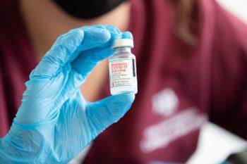 close up of a gloved hand holding a vial of the moderna covid-19 vaccine