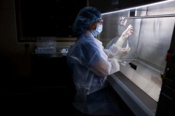 a woman wearing scrubs and protective gear prepares a vaccine