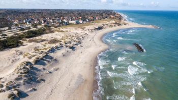 an ocean coastline with sand dunes separating the water from homes