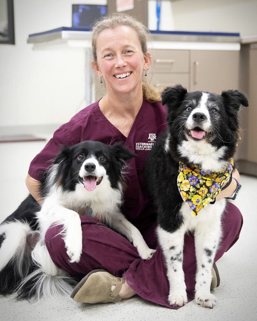 kate creevey sitting on the floor holding two black and white dogs