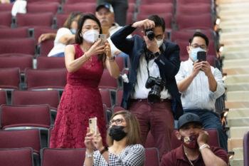 family members sitting in the stands stand up and take photos of graduates