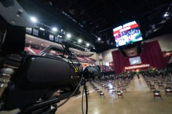 a large camera points toward the empty floor of reed arena before a commencement ceremony
