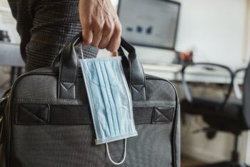 closeup of a young man in an office holding a briefcase and a surgical mask in his hand