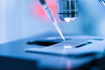 Picture of scientist dropping chemical liquid on the slide at microscope