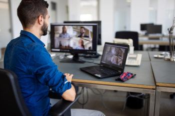Businessman video conferencing with team on computer. Young man discussing project details with team via video call.