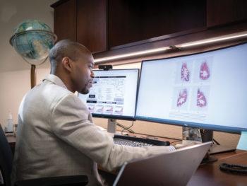portrait of martial ndeffo in his office sitting in front of two computer monitors