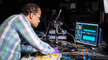 photo of man in lab working at a table filled with equipment and a computer monitor