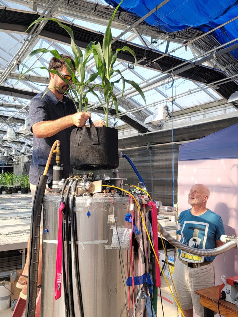 a man stands above the device holding a basket containing a plant
