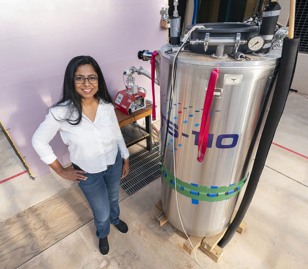 a woman stands in a greenhouse next to a large silver piece of equipment