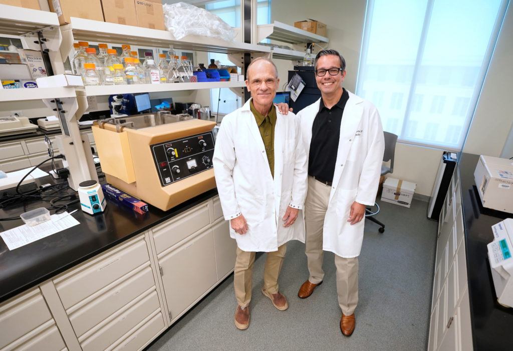 two men in white lab coats standing side by side in a laboratory