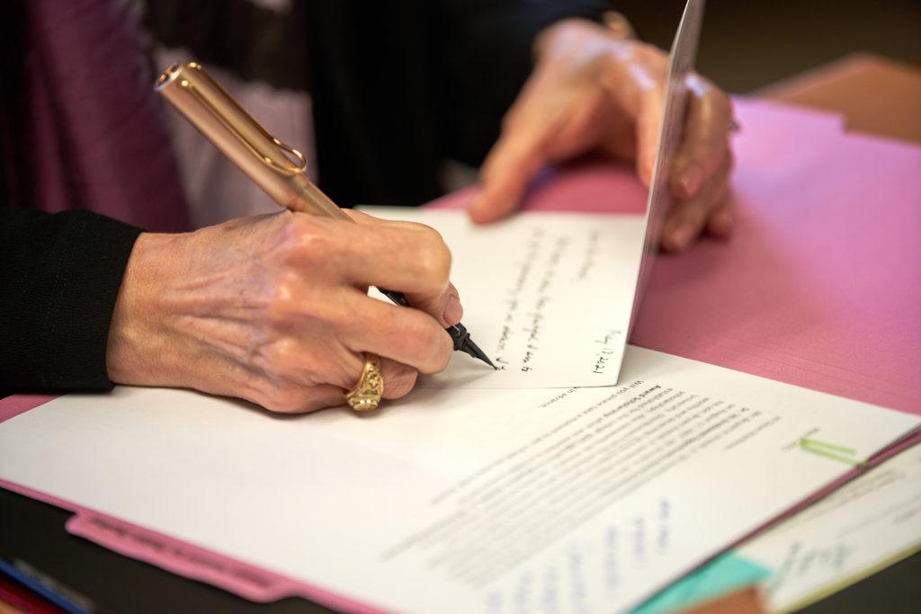 close up of matthew writing a note with a gold pen at her desk