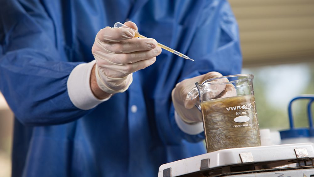 a person wearing a blue shirt holding a pipette over a beaker of solution