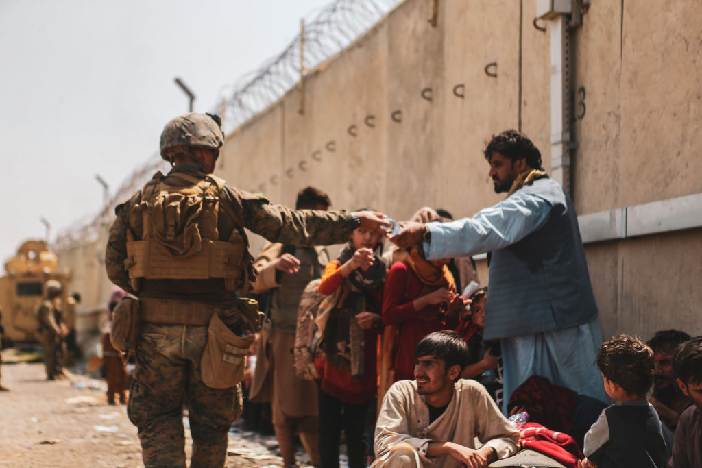 soldier hands out water to afghan evacuees outside an airport
