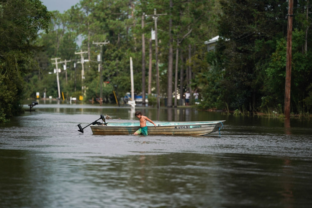 a boy pushes a boat as he walks through floodwater in a flooded street