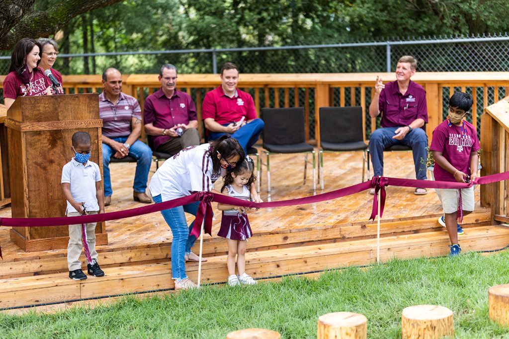 a woman helping a little girl cut the ribbon opening the playground