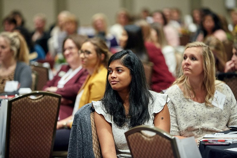 group of women sit at tables in a conference room