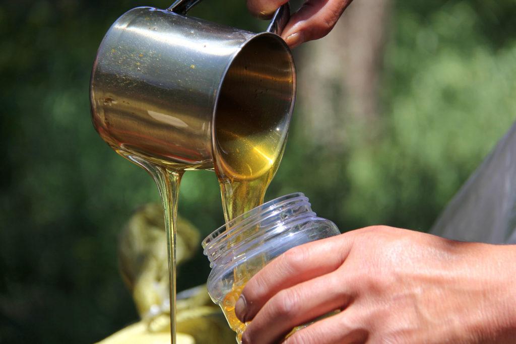 close up image of someone pouring honey into a glass jar