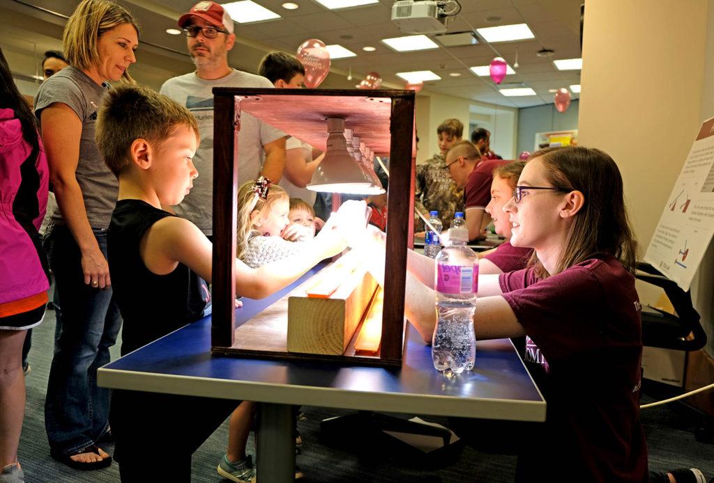 a student sits at a table speaking to young children and parents