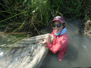 Woman standing in waist-deep water holding a small fish in one hand