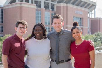 group photo of four students standing in front of kyle field