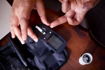 cropped shot of the hands of a person using a blood sugar testing device on one finger