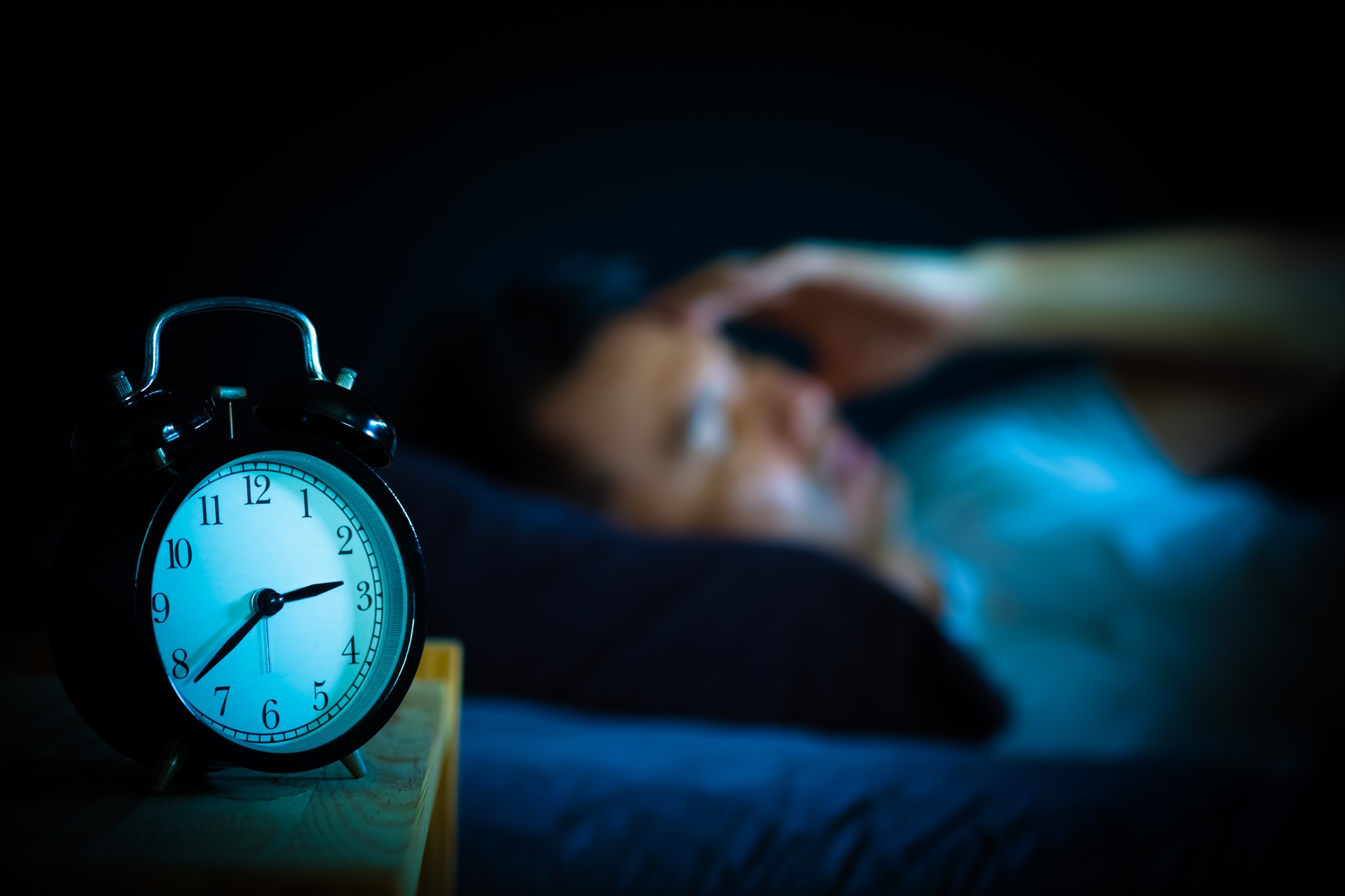 man laying in bed awake next to alarm clock in the middle of the night
