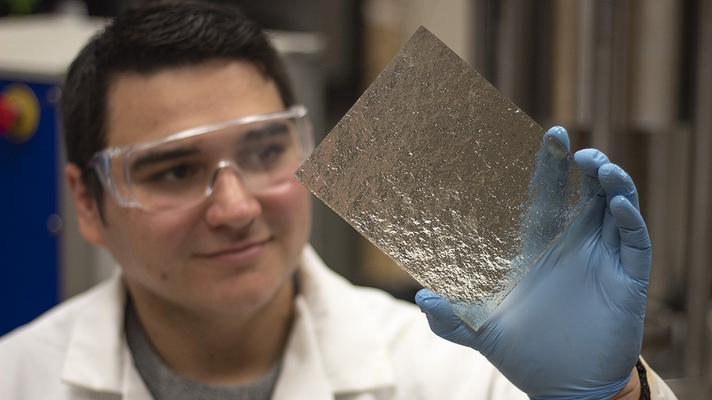 student wearing goggles in the lab holding up a shiny silver object