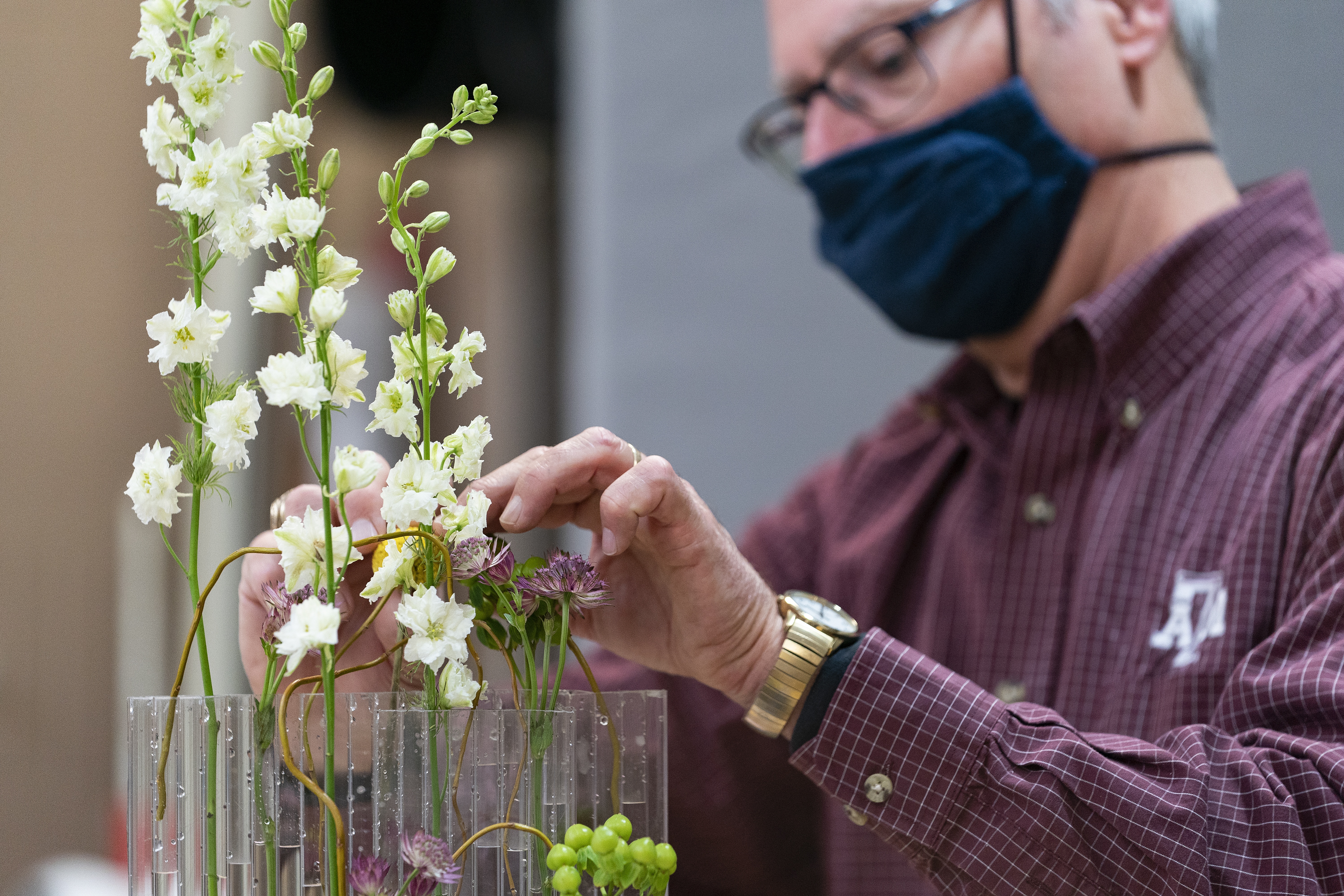 a man wearing a blac kface mask arranges flowers