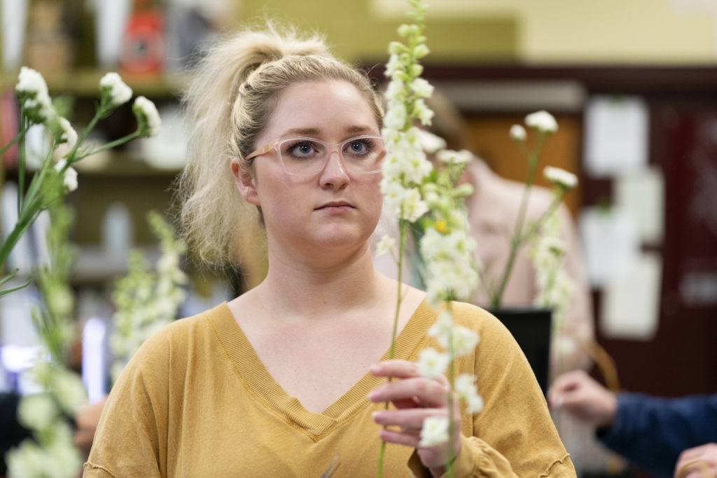 a female student wearing a yellow shirt holds up a stem with white flowers