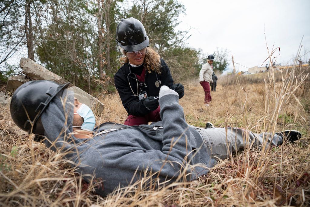 a female student kneels next to a male student in a field during a wildfire simulation