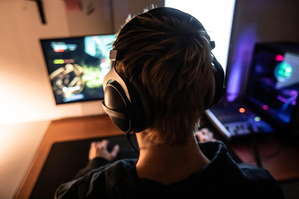 Rear View of Gamer with Headset on Playing Online Video Games in Dark Room