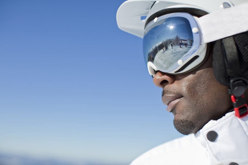 close up of a black man wearing a ski mask with the mountain reflected in his goggles