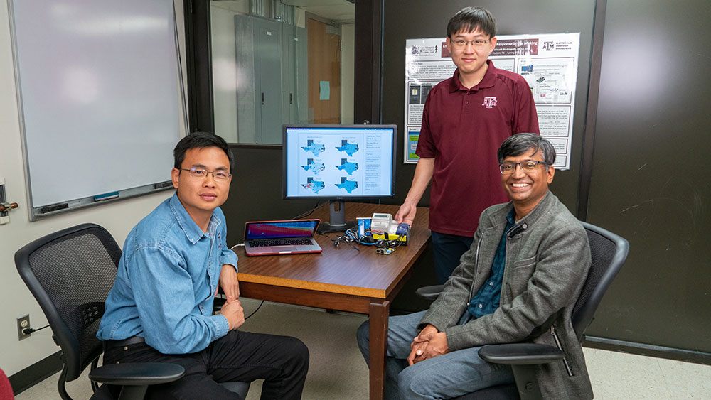 group photo of three researchers standing and sitting around a table