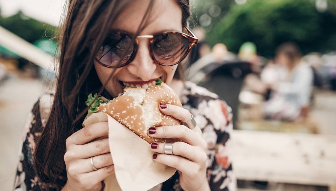 woman dining outdoors biting into a hamburger