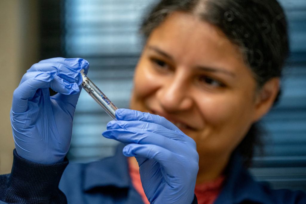 a photo of a woman holding a test tube between her gloved hands and smiling