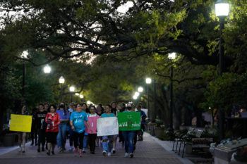 a large group of students walk through campus at night holding signs