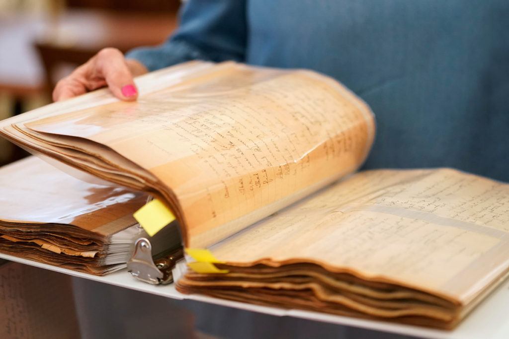 a woman turns the pages of a thick binder containing old letters in plastic covers