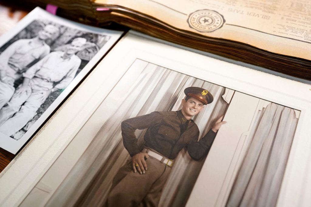 photos and documents are spread out on a table. the photo in focus is a colorized portrait of a man in a texas a&m corps of cadets uniform