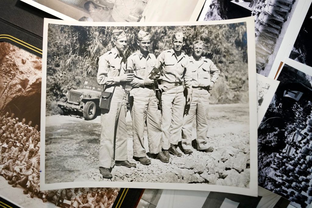 a black and white photo of four men in army uniforms sits on top of an assortment of other old photographs on a table