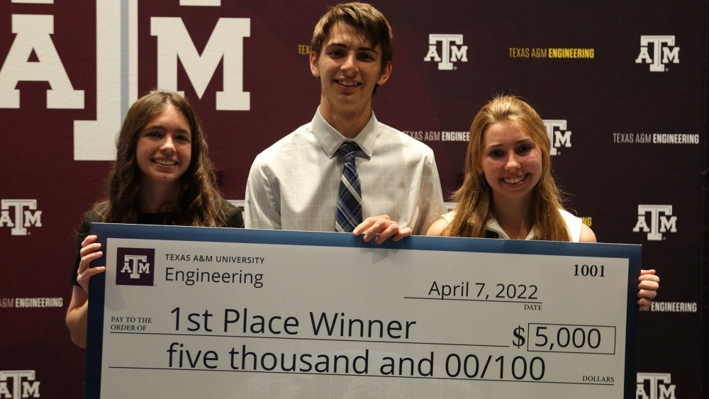 three students hold an oversized check for their first place win, with a $5,000 total