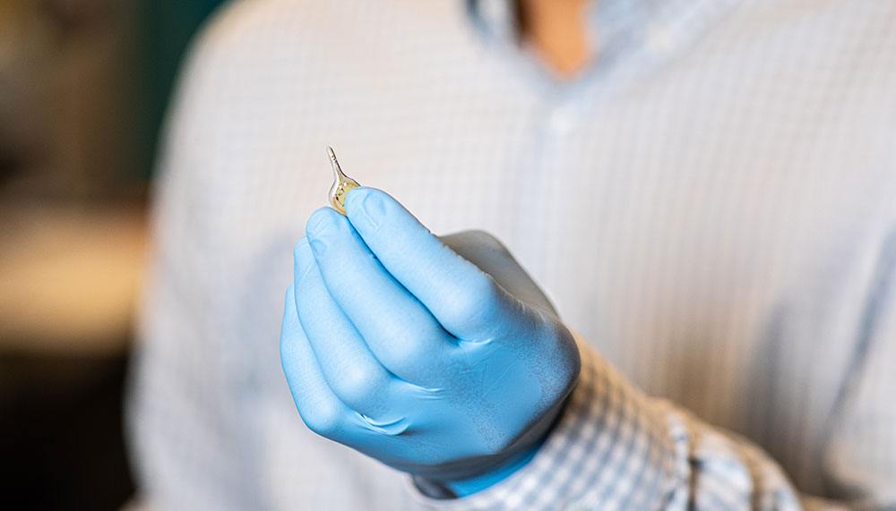 a photo of a gloved hand holding a small teardrop-shaped metallic device