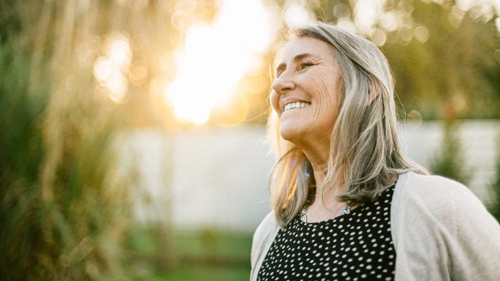 portrait of a senior woman smiling outdoors with a sunset behind her
