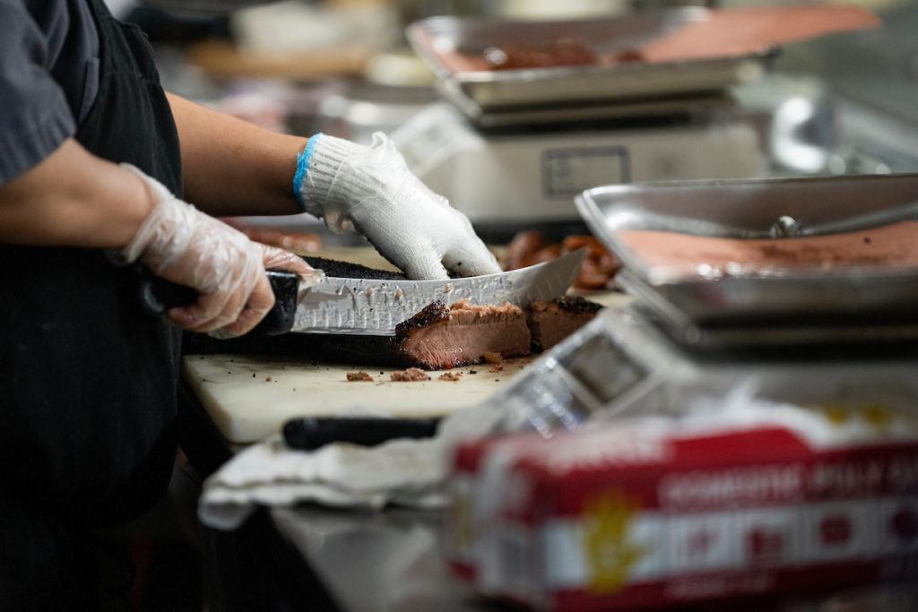 shot of a man wearing gloves slicing into brisket with a knife
