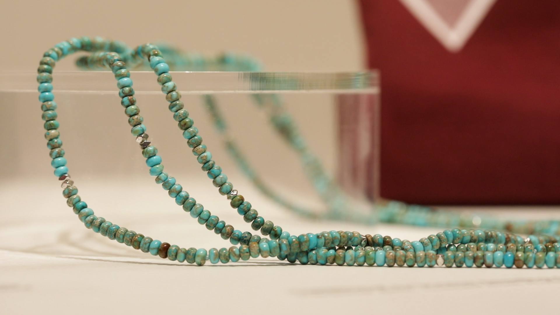 a photo of a several strands of turquoise beads on a transparent pedestal