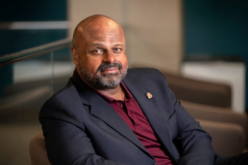 a photo of a man in a maroon polo and a black suit jacket sitting down and looking into the camera