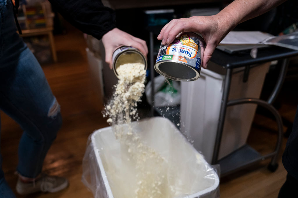 staff pour cans of powdered baby formula into a trash can