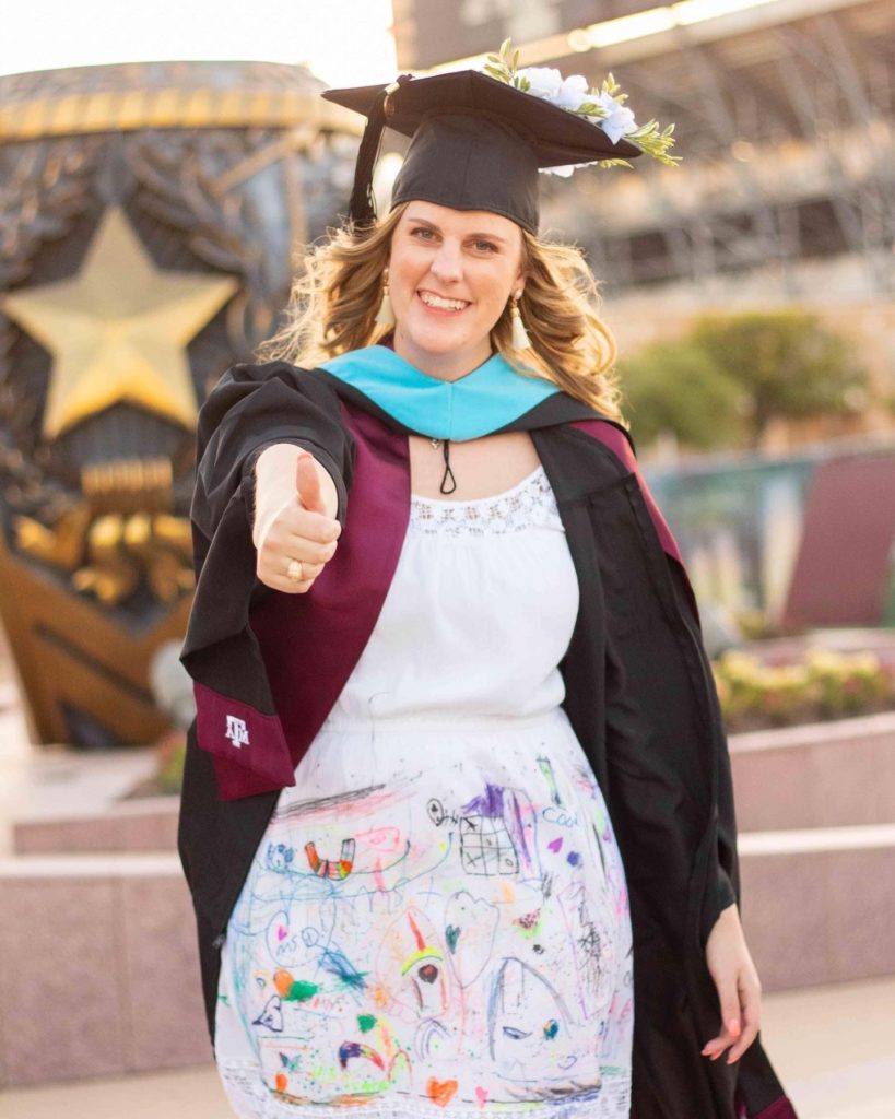 margaret teague stands in her cap and gown wearing a white dress covered in colorful drawings by her students